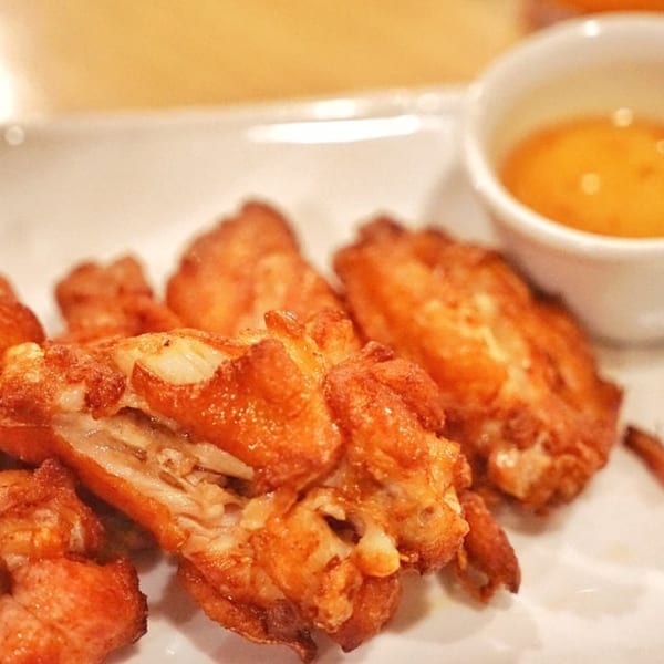 Crispy fried Thai chicken wings with a side of dipping sauce on a white plate.
