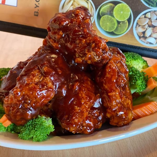 Sweet and sour chicken wings with broccoli and carrots on a white plate at Thai Time.