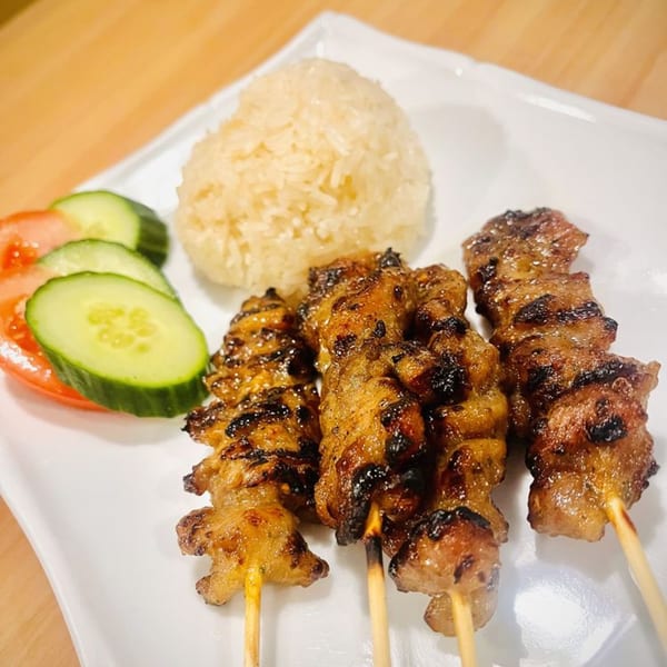 Grilled Thai chicken skewers with sticky rice, cucumber, and tomato slices on a white plate.