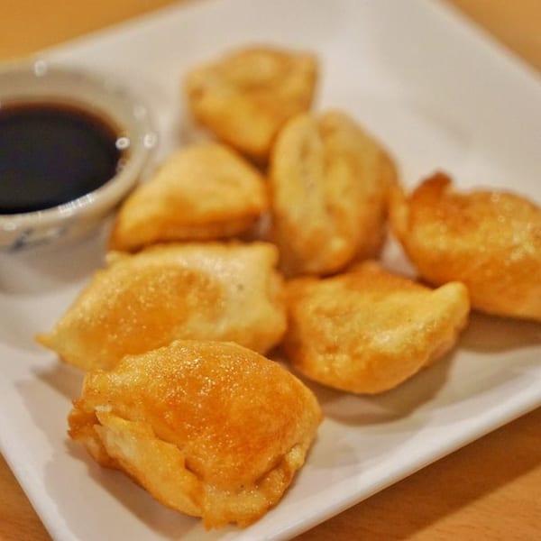 Golden-fried Thai dumplings with a side of dark dipping sauce on a white plate.