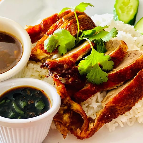 Crispy duck slices with cilantro on a bed of white rice, served with two dipping sauces and cucumber.