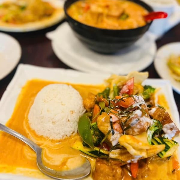 Thai red curry with rice, vegetables, and tofu, served with a spoon.