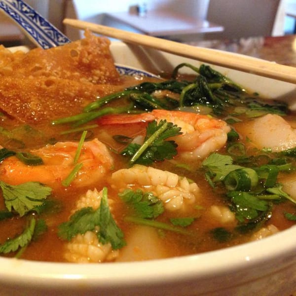 Close-up of a Thai seafood soup with shrimp, squid, cilantro, and crispy wonton.