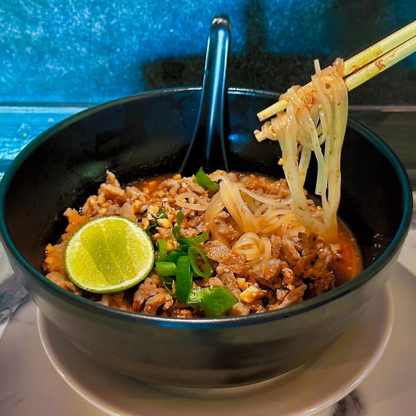 Chopsticks lifting noodles from a bowl of Thai Time's spicy minced pork with lime and scallions.
